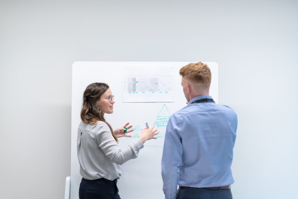 Two people standing in front of whiteboard discussing something.